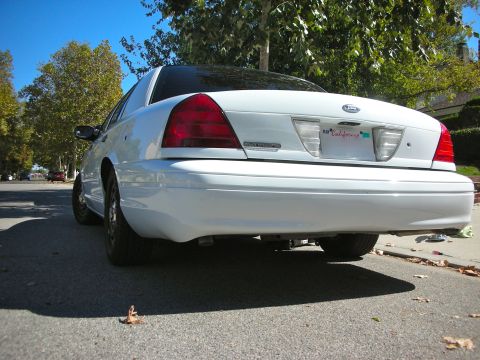 2004 Ford Crown Victoria - A white sedan is parked on the street, showing its rear end and taillights under a clear blue sky.