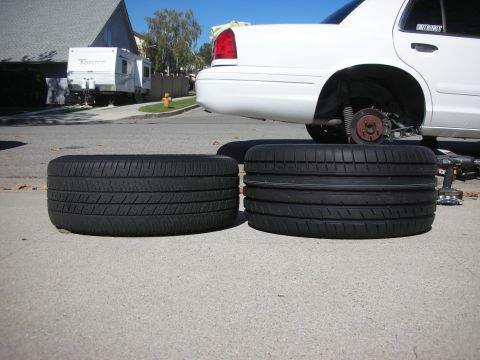 2004 Ford Crown Victoria - A white car's rear wheel is off, with two tires placed on the ground nearby.