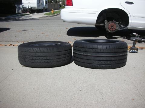 2004 Ford Crown Victoria - A comparison of two tires, with one mounted on a rim, beside a 2004 Ford Crown Victoria undergoing a wheel change.