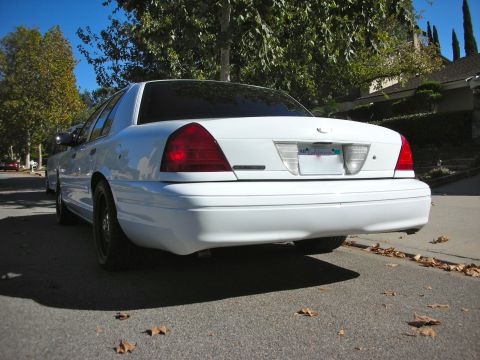 2004 Ford Crown Victoria - A white 2004 Ford Crown Victoria is parked on a street with fallen leaves on the ground.