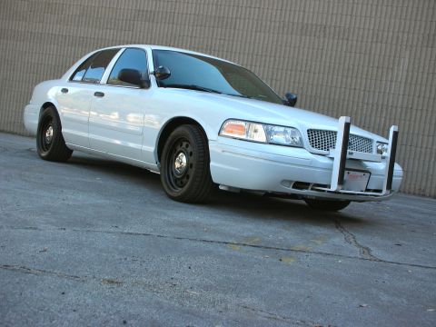2004 Ford Crown Victoria - A white 2004 Ford Crown Victoria police car is parked in front of a textured wall.