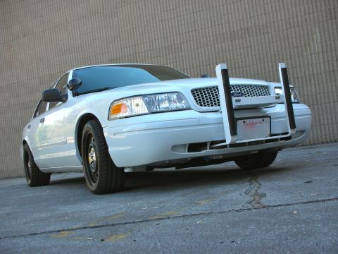 2004 Ford Crown Victoria - A white 2004 Ford Crown Victoria police car is parked in front of a textured wall, equipped with a front push bar.