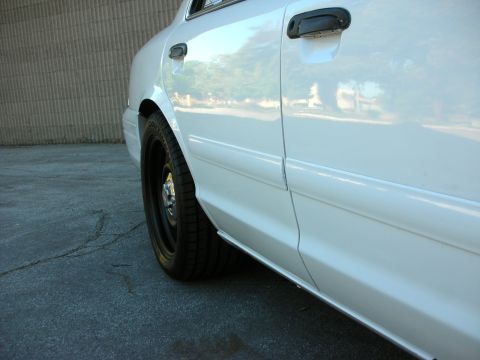 2004 Ford Crown Victoria - Side profile of a white 2004 Ford Crown Victoria, highlighting its black wheels.
