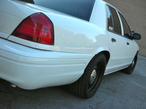 2004 Ford Crown Victoria - The rear section of a white sedan is shown, focusing on the taillight and rear wheel.