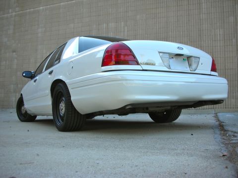 2004 Ford Crown Victoria - Rear view of a white sedan parked outdoors against a textured wall.