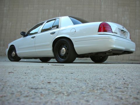 2004 Ford Crown Victoria - A white 2004 Ford Crown Victoria is seen from a low angle, highlighting its rear end and steel wheels.