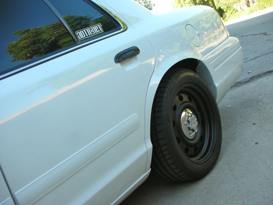 White 2004 Ford Crown Victoria rear quarter panel and wheel, showing a sticker on the rear window