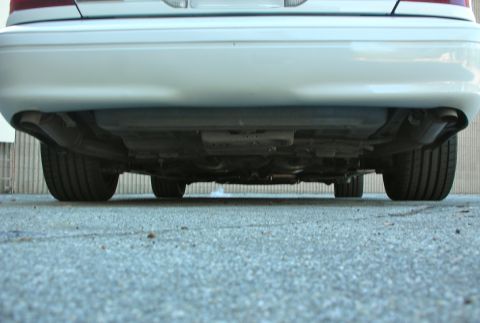 2004 Ford Crown Victoria - The rear underside of a white 2004 Ford Crown Victoria is visible, highlighting the exhaust system and tires.