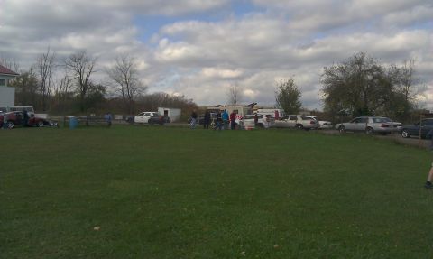 2007 Ford Crown Victoria - A group of vehicles are parked in an open field with a building and trees in the background.