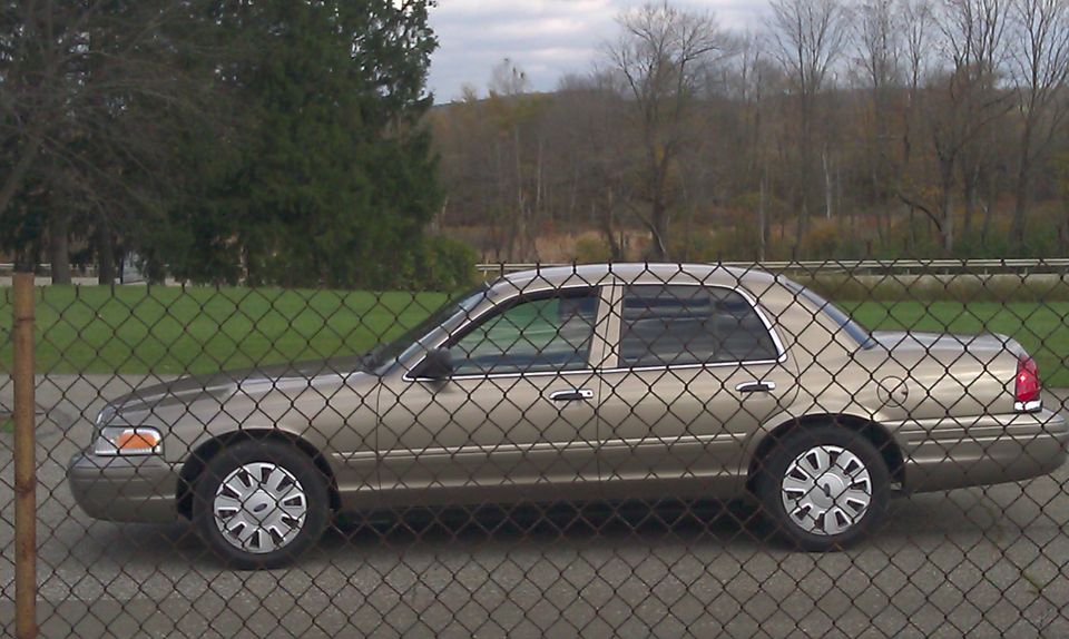 Tan 2007 Ford Crown Victoria parked behind a chain-link fence