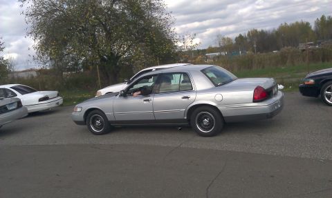2007 Ford Crown Victoria - A silver sedan is parked in a lot with other vehicles under a cloudy sky.