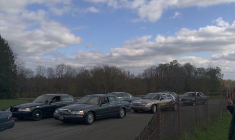 2007 Ford Crown Victoria - Multiple Ford Crown Victoria police cars are parked in a line on a road with trees in the background.