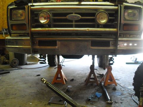 1986 Ford Bronco - The front of a Ford Bronco is shown on jack stands, with its grille and headlights visible.