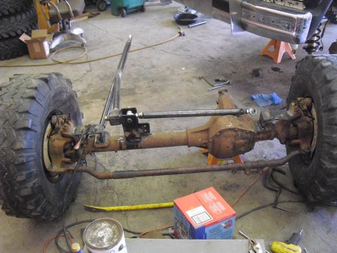 1986 Ford Bronco - The front axle and suspension of a vehicle are shown in a workshop setting, with large tires mounted.