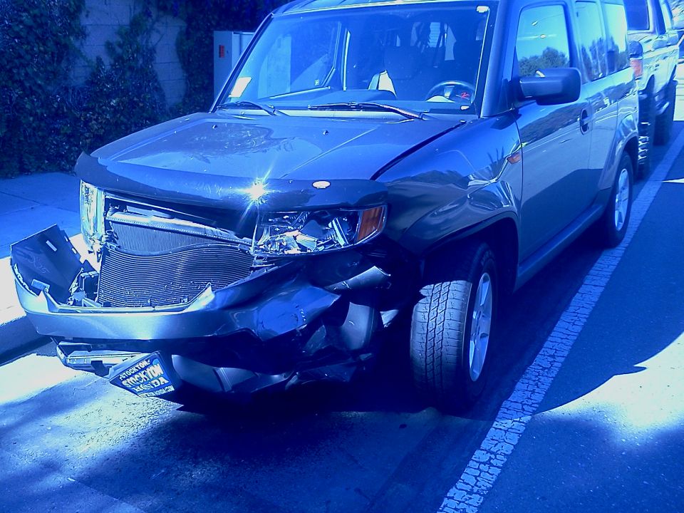 Dark SUV with heavily damaged front end, including grille and bumper. License plate visible