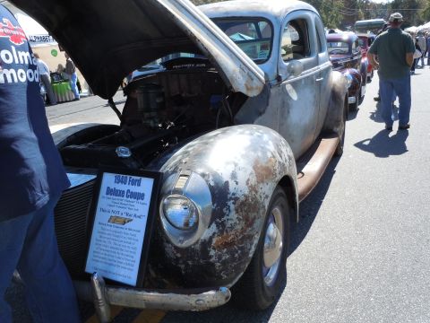 1979 Chevrolet Camaro - A weathered 1940 Ford Deluxe Coupe is displayed with its hood open, a descriptive sign in front.