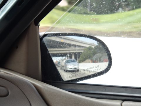 1993 Ford Taurus - Traffic viewed in the side mirror on a highway, with an overpass visible in the reflection.