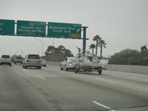 1993 Ford Taurus - A sedan tows a sailboat on a trailer down the highway under an overcast sky.