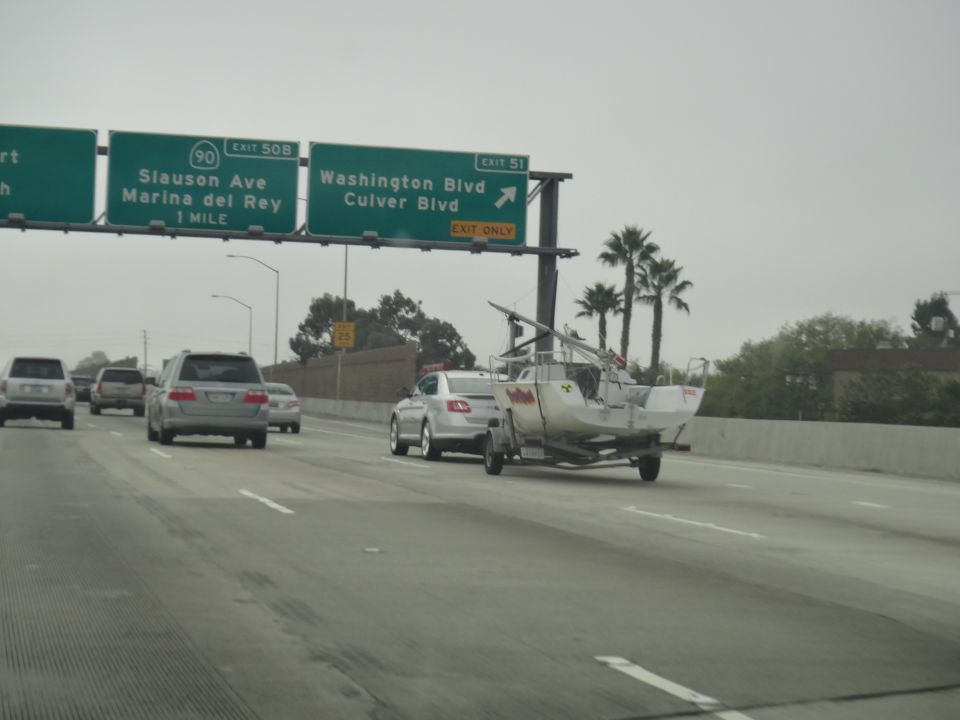 Silver sedan towing a white boat on a trailer on the freeway