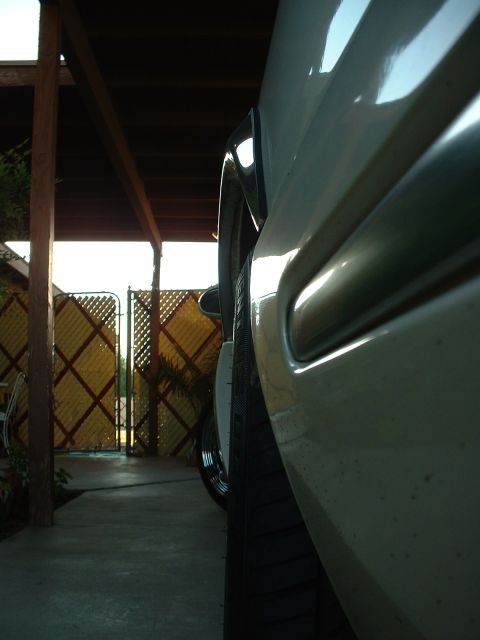 1997 Mercury Cougar - A close-up side view of a car's body panel and tire, with a fence and carport in the background.