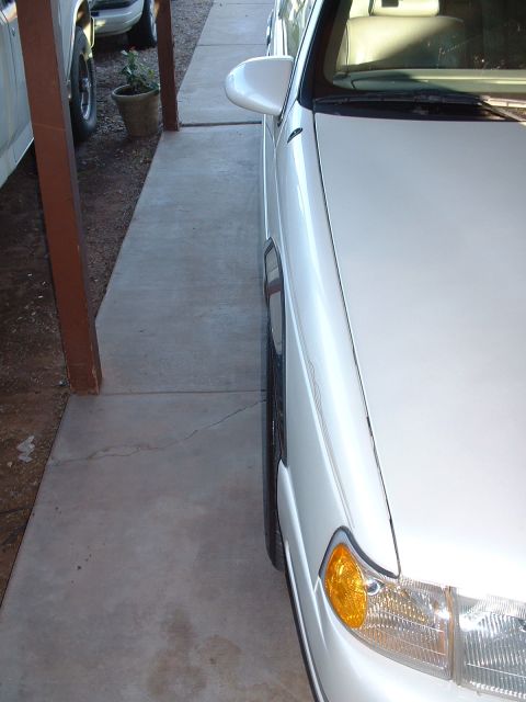 1997 Mercury Cougar - A white sedan is parked next to a pickup truck, with a concrete walkway running alongside.