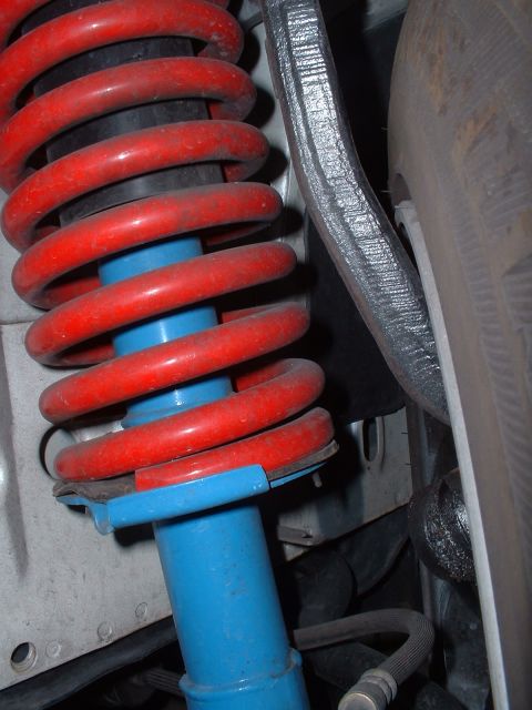 1997 Mercury Cougar - Close-up view of a red coilover suspension system with a blue shock absorber body, partially obscuring a tire.