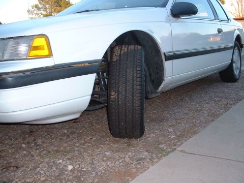 1997 Mercury Cougar - Close-up view of the front suspension and tire of a white coupe.