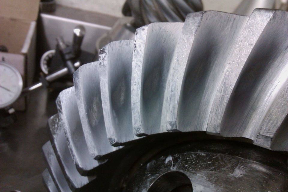 Close-up of a differential gear set with visible wear on the teeth. A dial indicator is in the background
