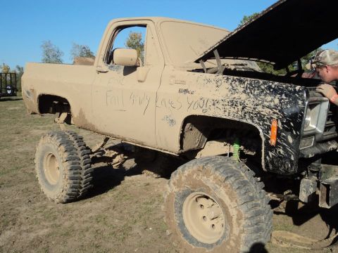 1995 Ford Bronco - A mud-splattered pickup truck sits in a dirt lot with its hood open and writing on the side.