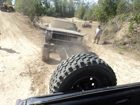 1995 Ford Bronco - A lifted truck navigates a muddy off-road course with other vehicles present.
