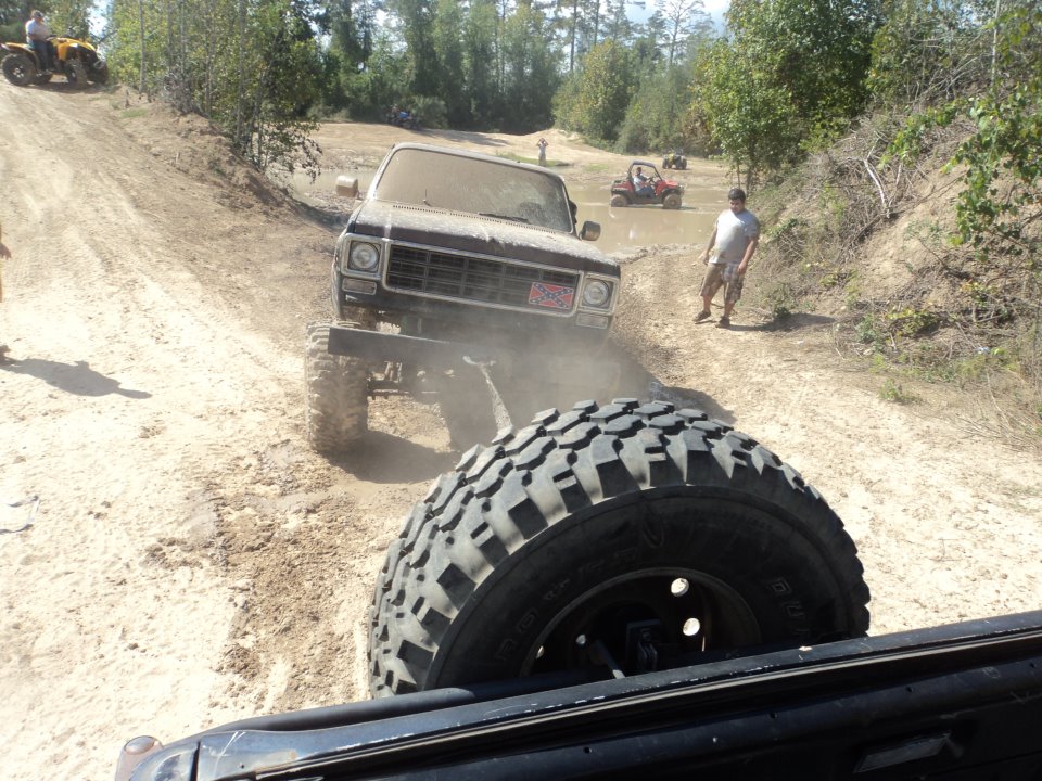 Muddy lifted truck driving on dirt path, another vehicle behind it