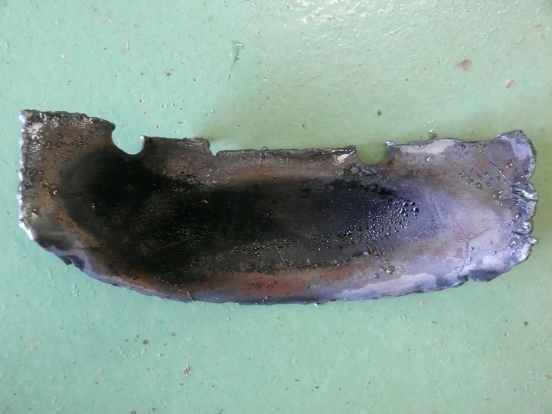 Fragment of burnt metal with rough edges, resting on a green surface