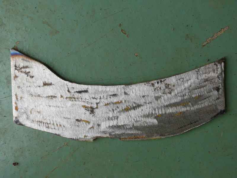 Curved metal fragment with grind marks on a green surface