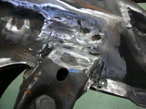 1976 Chevrolet Corvette - Close-up view of a heavily damaged and welded metal frame component, likely from a vehicle undergoing repair or restoration.