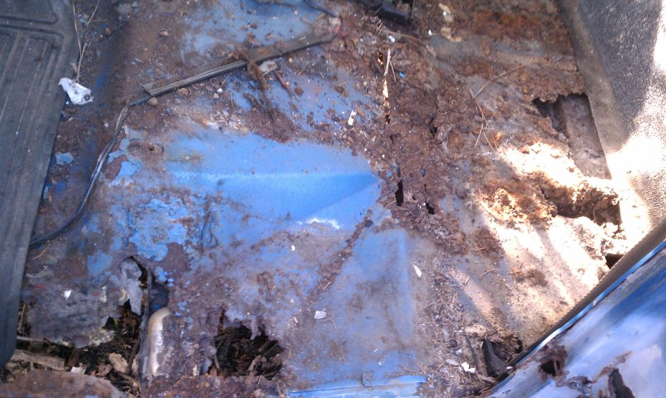severely rusted blue floor pan with holes and debris
