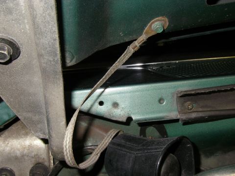 1990 Ford Bronco - Close-up of a flat braided metal ground strap with round terminal ends, one bolted to a green-painted body panel and looping down toward th…