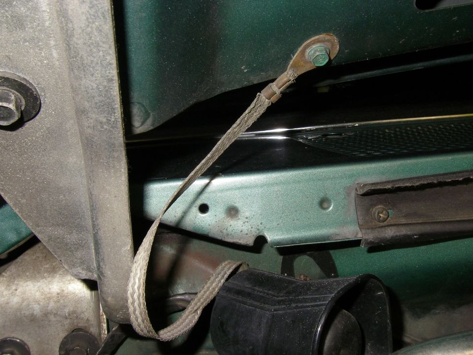 Braided ground strap bolted to green body panel with visible frame and terminal ends