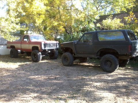 1986 Ford Bronco - Two modified off-road vehicles, a Ford Bronco and a pickup truck, are parked side-by-side.