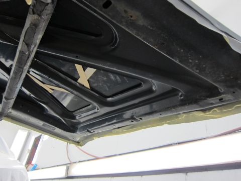 1987 Dodge 1500 - The underside of a car hood is shown, with masking tape applied to the edges and some wooden wedges placed on the bracing.