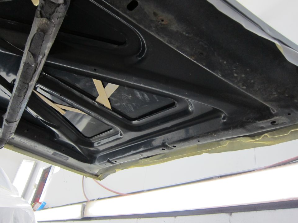 underside of a car hood with tape and some wooden wedges