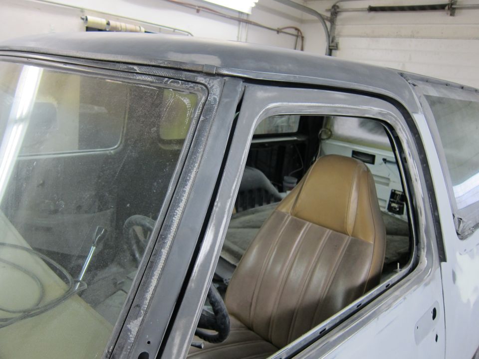 Truck interior with tan seats and black steering wheel, viewed from the passenger side door opening. The vehicle is undergoing repairs
