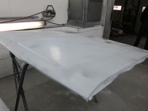 1987 Dodge 1500 - A vehicle hood is prepped for painting, resting on a stand in a workshop environment.