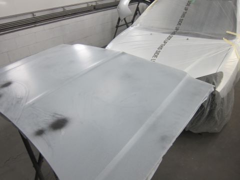 1987 Dodge 1500 - A car hood is prepped for painting, with the rest of the vehicle covered in plastic.