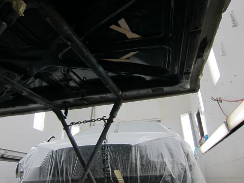1987 Dodge 1500 - A vehicle's undercarriage is visible while another vehicle is covered in plastic in a workshop.