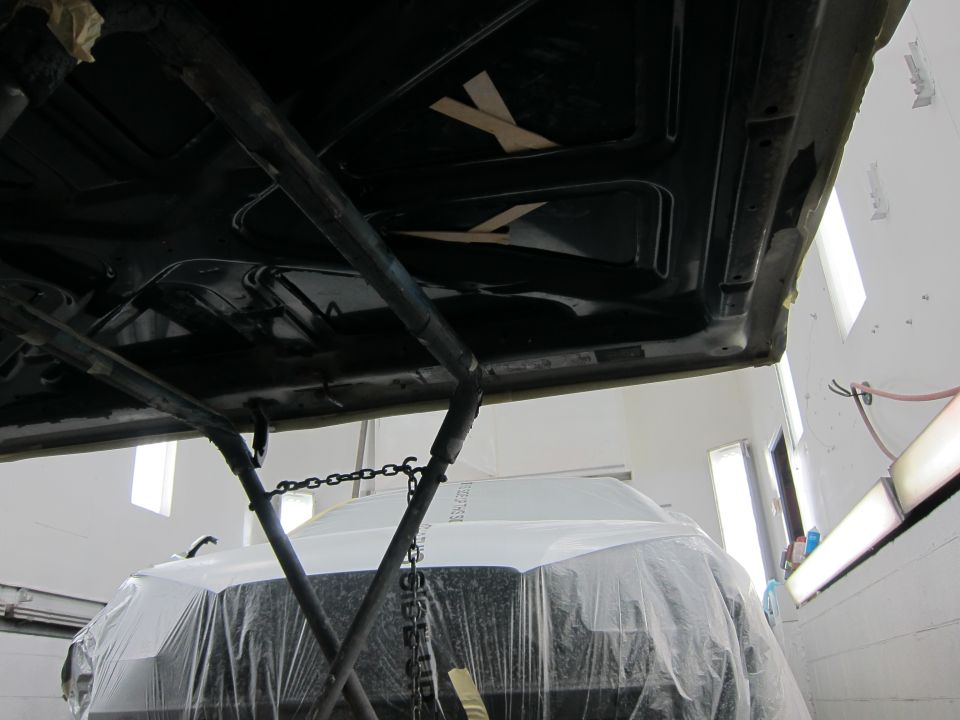 Underside of a vehicle being worked on, with another vehicle covered in plastic below