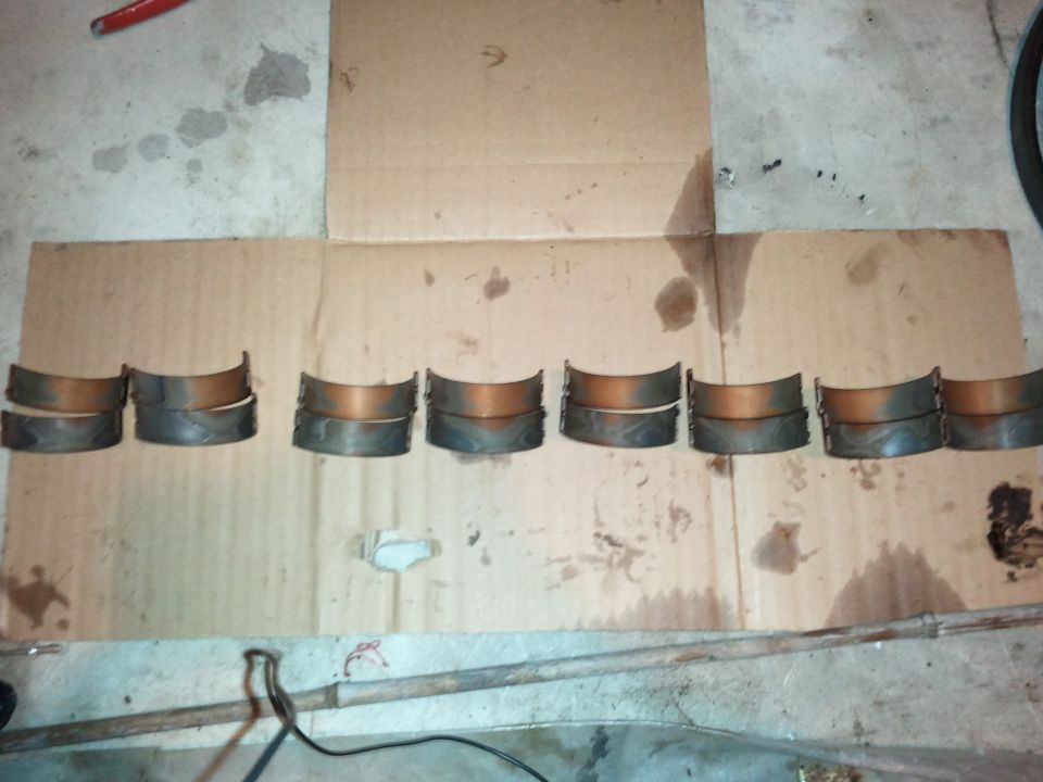 Eight pairs of worn engine bearing shells laid out on cardboard in a garage