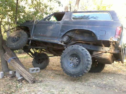 1986 Ford Bronco - This heavily modified SUV appears to be stuck on a log, with its front wheel elevated.