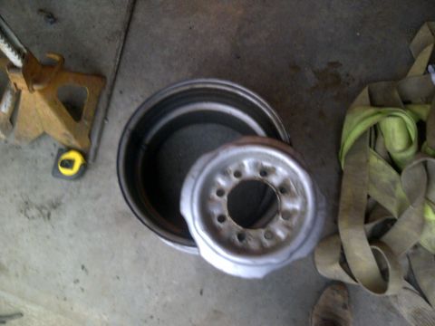 1979 Ford E250 - A steel wheel rim and a larger metal rim are on a concrete floor next to a yellow jack stand and green straps.
