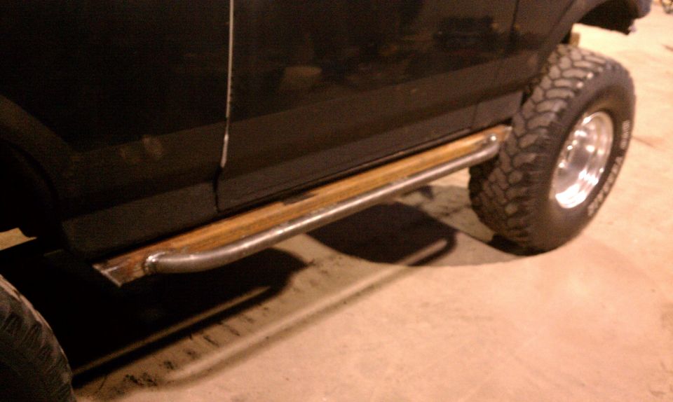 Black SUV side view with custom metal and wood rock sliders and off-road tires
