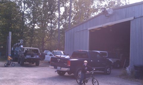 1979 Ford Bronco - A group of vehicles, including a pickup truck and an SUV, are parked outside a barn on a sunny day.